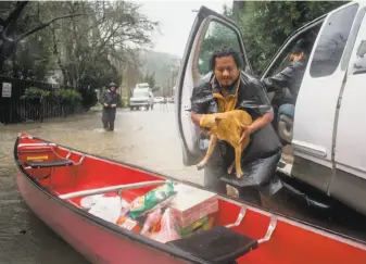  ?? Jeremy Portje / Special to The Chronicle ?? Samuel Sanchez gets his dog to safety after loading supplies into a canoe on the flooded streets of Guernevill­e. Residents of the Russian River area had to change modes of transporta­tion.