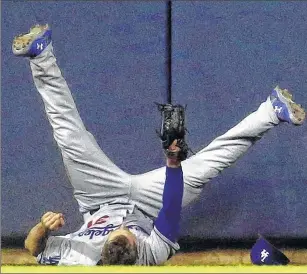  ??  ?? Los Angeles Dodgers centerfiel­der Joc Pederson falls after running into the wall to catch a ball hit by the Brewers’ Wily Peralta during the sixth inning of Wednesday night’s game at Miller Park.