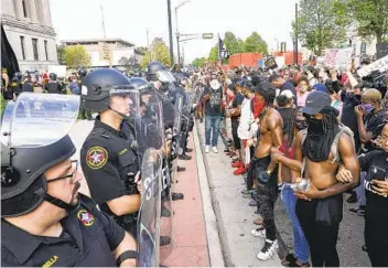  ?? MORRY GASH AP ?? Protesters link arms Monday in front of a police line outside the Kenosha County Courthouse in Kenosha, Wis., after violence broke out following the shooting of a Black man by police officers.