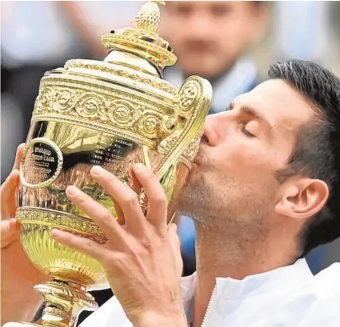  ?? // REUTERS ?? Djokovic, ayer, besa el trofeo de campéon de Wimbledon