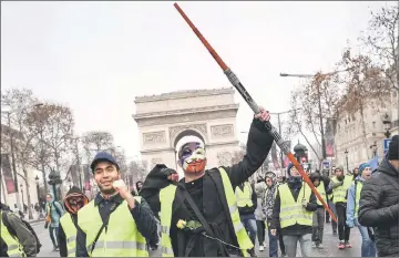  ??  ?? A man wearing an Anonymous mask and a yellow vest (gilet jaune) and holding a Star Wars Jedi light laser takes part in a demonstrat­ion to protest against rising costs of living they blame on high taxes, by the Arc de Triomphe in Paris. — AFP photo