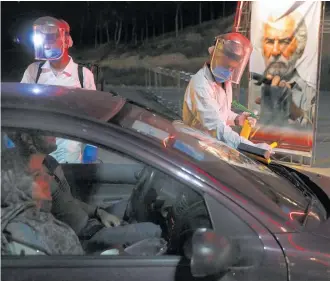  ?? Photo / AP ?? Workers wearing protective suits disinfect cars against coronaviru­s while people enter a new drive-in cinema in a carpark near the Milad telecommun­ications tower.