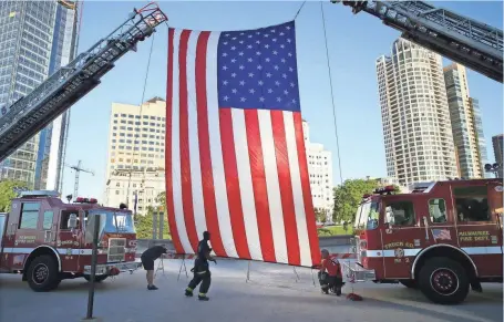  ?? MICHAEL SEARS / MILWAUKEE JOURNAL SENTINEL ?? Members of the Milwaukee Fire Department raise a large American flag Sunday between two aerial ladder trucks during the “Milwaukee County Remembers 9/11” memorial service at the Milwaukee War Memorial Center. For more photos, go to jsonline.com/news.