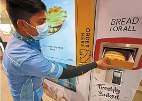  ?? ?? a man collecting food from a vending machine that gives out free bread in dubai. — AFP