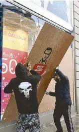  ?? REUTERS ?? A protester stands next to burning trash bins on a street during clashes with police at a national day of protest by the ‘yellow vests’ movement in Paris on Saturday (right) while workmen place a wood panel to protect a broken window at a clothing store the day after clashes (below).