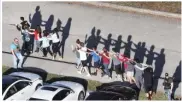  ?? JOE RAEDLE/ ?? TOP: Students released from a lockdown embrace following the shooting at Marjory Stoneman Douglas High School Wednesday in Parkland, Florida.
ABOVE: Students are brought out of the school after the shooting that killed at least 17 and injured more...