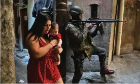  ?? Photograph: Carl de Souza/AFP/Getty Images ?? In this file photo taken on 23 September 2017 a woman walks with her baby past a militarize­d police soldier in the Rocinha favela in Rio de Janeiro, Brazil.