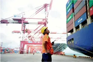  ?? — AP ?? A worker watches as shipping containers are loaded onto a ship at a port in Qingdao in China.