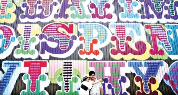  ?? THE YOMIURI SHIMBUN ?? A pair takes a selfie in front of British artist Ben Eine’s colorful work, which is painted on the outside wall of a former iron factory in Osaka.