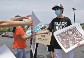  ??  ?? A community member passes out posters before the start of a car caravan to Danville to protest for police reforms in Contra Costa County.