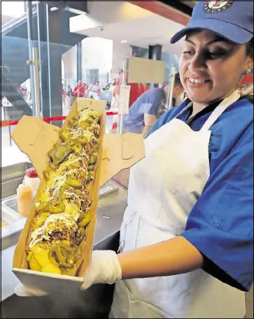  ??  ?? Fabiola Bolanos shows off a freshly made Most Valuable Tamale before a game between the Los Angeles Angels and the Texas Rangers on April 28 in Arlington, Texas. The 24-inch tamale is filled with the boomstick hot dog, and topped with Texas chili,...