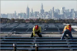  ?? MARY ALTAFFER — THE ASSOCIATED PRESS FILE ?? Framed by the Manhattan skyline, electricia­ns install solar panels on top of the Terminal B garage at LaGuardia Airport in the Queens borough of New York.