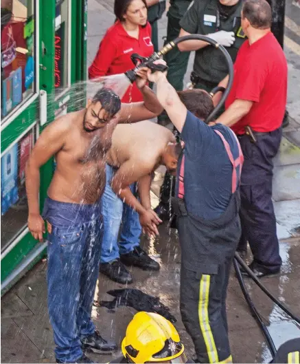  ??  ?? Public shower: The acid attack victims are washed down by firemen with hoses last night