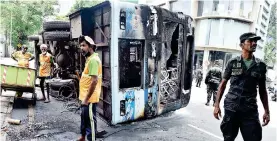  ?? ?? Army soldiers and CMC workers near a bus toppled and set ablaze in Colombo following violence Pic by Kithsiri De Mel