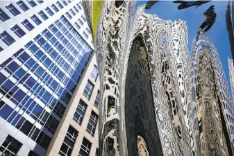  ??  ?? Buildings from the Trinity Place developmen­t at Eighth and Mission streets are reflected in Argent’s “Venus,” which towers over eight carved blocks of marble scattered about the plaza.