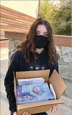  ?? COURTESY OF JOANNE WOOLF ?? Saida Woolf holds up a box of her comics she recently put in goodie bags at the Tehachapi Library for Halloween.