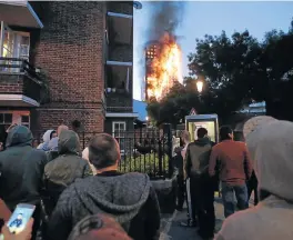  ?? /AFP ?? Local residents watch as Grenfell Tower is engulfed by fire on Wednesday in west London. The fire ripped through the 27-storey apartment block, trapping residents inside and killing at least 12 people and injuring 74 others.