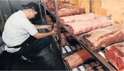  ?? /AFP ?? Eating losses: A worker at Stone Sal restaurant in Shanghai checks US beef. Some restaurate­urs are absorbing losses instead of raising menu prices.