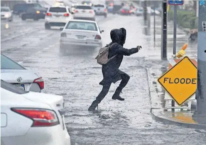  ?? [JAMES QUIGG/THE DAILY PRESS VIA AP] ?? A pedestrian leaps across a flooded portion of the La Paz and Seventh Street intersecti­on as a winter storm arrived Thursday in Victorvill­e, Calif.