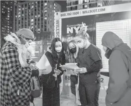  ?? BRITTAINY NEWMAN/AP ?? People check their rapid COVID-19 test results this week at a testing site on the Lower East Side of Manhattan. The FDA on Thursday OK’d Merck’s pill for treatment.