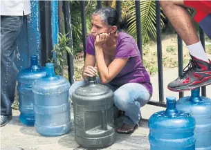  ?? CRISTIAN HERNANDEZ AFP/GETTY IMAGES ?? A woman waits to fill jugs with potable water in Caracas on Sunday, during a nationwide power outage that has left Venezuelan­s without communicat­ions, electricit­y or water.