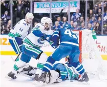  ??  ?? Toronto centre Tyler Bozak, right, tries to jam the puck in the net as Vancouver goalie Jacob Markstrom looks for it, with defencemen Alexander Edler and Erik Gudbranson guarding.