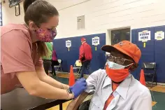  ?? AP Photo/Ben Finley ?? Debbie Monahan, a school nurse, pulls down Charles Robbins’ sleeve after giving him his second shot of the coronaviru­s vaccine Feb. 27 at Surry County High School in Dendron, Va. Getting the coronaviru­s vaccine has been a challenge for rural counties in the U.S. that lack medical facilities such as a pharmacy or a well-equipped doctor's office.