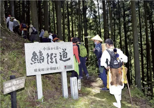  ?? Yomiuri Shimbun photos ?? Hikers walk the Harihatago­e road at an event in Obama in May. The signboard says “Saba-kaido” in large letters.