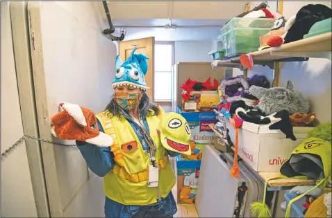  ??  ?? Erickson tries on her “Headache Hat” (a shark with its mouth around her head) as she sorts through the boxes of hats she has accumulate­d over the years at Hawthorne Elementary School.