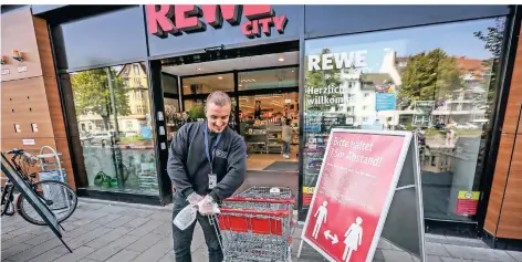  ?? FOTO: HANS-JUERGEN BAUER ?? Desinfizie­rt die Einkaufswa­gen: Lukas Strungat von der Firma MTS Security beim Rewe-Markt an der Theo-Champion-Straße in Oberkassel.