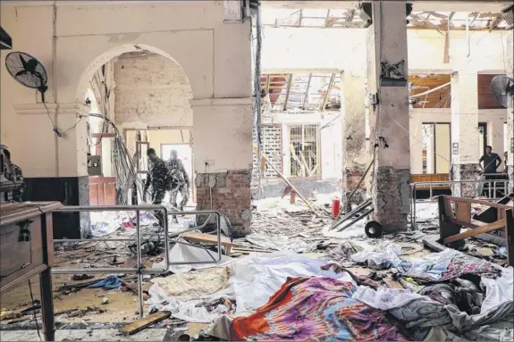  ?? Ishara S. Kodikara / AFP ?? Sri Lankan security personnel walk next to dead bodies on the floor amid blast debris at St. Anthony’s Shrine following an explosion in the Sri Lankan church on Sunday. A string of blasts ripped through high-end hotels and churches holding easter services in the island country killing at least 280 people.