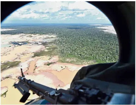  ??  ?? Blight on the environmen­t: A soldier in a helicopter scanning a chemically deforested area of the Amazon jungle caused by illegal mining activities in the river basin of the Madre de Dios region in southeast Peru. — AFP