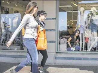  ?? RALPH BARRERA / AMERICAN-STATESMAN ?? Shoppers pass by as Silvia Mascorro (right) cleans a display window of the shop Papaya, a women’s clothing store located in the San Marcos Premium Outlets, on Wednesday afternoon. San Marcos city officials say that recent decreases in sales tax revenue...