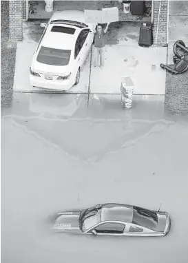  ?? Brett Coomer / Houston Chronicle ?? A man holds up a sign saying, “Bring Milk &amp; Beer” as floodwater­s creep close to a house last week in the Wimbledon Champions Park subdivisio­n.