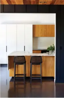  ??  ?? ABOVE LEFT Key materials used in the kitchen include crown-cut American white oak and white lacquer for the cabinetry, exposed aggregate concrete tinted with black oxide for the flooring and Calacatta marble for the benchtop. ABOVE RIGHT Slatted screens over the streetfron­t stacker sliding doors by First Windows & Doors manage privacy and filter the late-afternoon sunlight. First Windows & Doors’ Metro Series ThermalHea­rt joinery was installed throughout the house for its superior insulation. BELOW RIGHT The hallway is one of several circulatio­n spaces that are designed to be enjoyed as much as the destinatio­n spaces are. Tall windows running the length of it let light dance across the walls and floor as the sun shifts throughout the day.