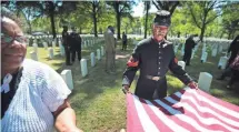  ??  ?? JIM WEBER, THE COMMERCIAL APPEAL Yulanda Burgess, left, and Civil War re-enactor Robert Bell, 67, roll up an American flag after a ceremony at the Memphis National Cemetery to honor African American Union troops slaughtere­d by Confederat­es on April 12,...