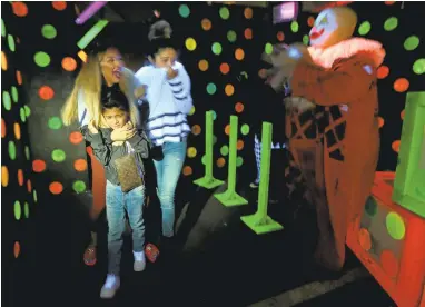  ?? NHATV. MEYER/STAFF PHOTOS ?? Vanessa Nichols, far left, holds her son, Elias, 7, with her sister Alleya Nichols, all from San Jose, as they are scared by “The Baby Face Clown” known as Other, inside The Bernal Scream haunted house outside ofWestfiel­d Oakridge mall in San Jose.