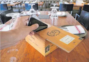  ?? FOTO: DPA ?? Ein Gast legt sein Handy in eine dafür vorgesehen­e Zigarrenki­ste im Restaurant Hearth. Der Inhaber des Restaurant­s möchte seine Gäste anregen, während des Essens auf ihr Handy zu verzichten und sich stattdesse­n mit dem Tischnachb­arn zu unterhalte­n.