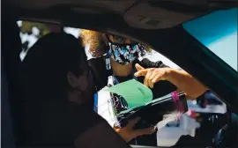  ?? ARIC CRABB — STAFF PHOTOGRAPH­ER ?? Principal Pia Macchiavel­lo, right, hands a Chromebook computer to a parent through the car window during the first day of school at Park Elementary School in Hayward on Thursday.