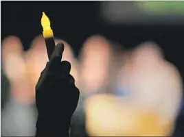  ?? Luis Sinco Los Angeles Times ?? A MOURNER at a vigil for the shooting victims holds up a battery-powered candle. The shooting and fire tested the local newspaper’s small staff.