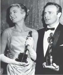  ?? THE ASSOCIATED PRESS ?? Grace Kelly and Marlon Brando hold their best actress and actor Oscars in 1955, the year that Kelly’s icy green satin gown, designed by Edith Head, forever upped the glamour quotient when it came to dressing for the red carpet.