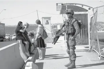  ?? MAYA ALLERUZZO/AP ?? An Israeli soldier secures a bus stop while Israeli settlers wait for a ride Thursday at the Gush Etzion transporta­tion hub for a number of West Bank Jewish settlement­s. Israeli settlers in the West Bank could soon face military rule.