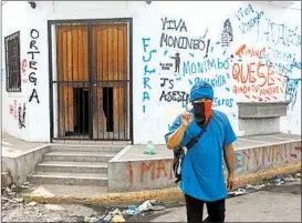  ?? ALFREDO ZUNIGA/AP ?? A masked pro-government militia member strolls past a house covered in anti-government graffiti Wednesday in the Monimbo neighborho­od of Masaya, Nicaragua.