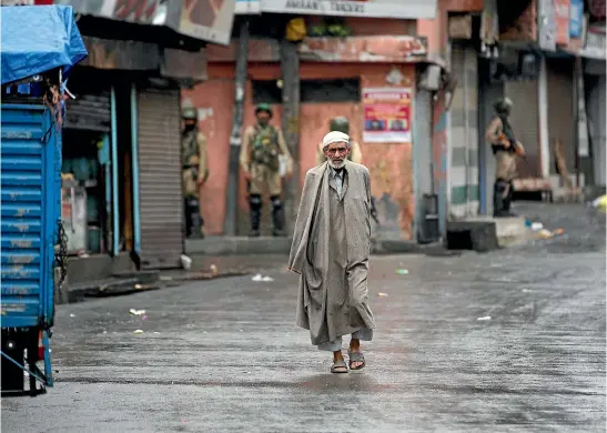  ?? AP ?? A Kashmiri man walks as Indian paramilita­ry soldiers stand guard during security lockdown in Srinagar, Indian-controlled Kashmir.