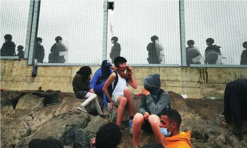  ?? EFE ?? Varios menores aguardan frente a la frontera de Ceuta, vigilada por la Policía Nacional, durante la avalancha de mayo