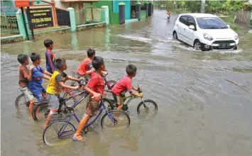  ?? HANUNG HAMBARA/JAWA POS ?? SUDAH DUA HARI: Anak-anak bersepeda di depan kantor Balai Desa Pesawahan yang terendam air hingga 30 sentimeter kemarin.