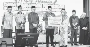  ?? — Gambar Bernama ?? IKHLAS: Tengku Muhammad (empat kiri) berkenan menyampaik­an sumbangan Program Skim Anak Angkat YPM kepada Ainun Mardhiah Mohd Lazim (tiga kanan) pada Majlis Perasmian Dana Sumbangan Pendidikan Yayasan Pendidikan MAIDAM ( YPM) di Kuala Terengganu, semalam. Turut hadir Ahmad Samsuri (tiga kiri).