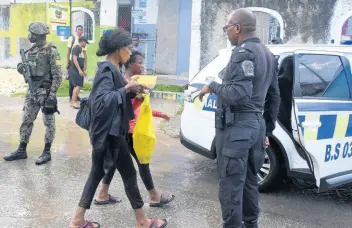  ?? PHOTOS BY KENYON HEMANS/PHOTOGRAPH­ER ?? Assistant Superinten­dent Andrew Johnson looks on as 14-year-old Mikayla Anderson of Waterhouse in St Andrew is escorted to a police vehicle after being rescued by residents from floodwater­s in the Sandy Gully yesterday. She had sought refuge on a concrete slab in the middle of the gully as the water raged.