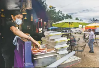  ?? MORGAN TIMMS/Taos News ?? Orlando’s employee Andrea Ramirez packs to-go boxes Wednesday (July 15) as guests enjoy their meals outside the local restaurant. The south parking lot was converted to additional seating as a way of adapting to the new restaurant rule that cuts indoor dining completely.