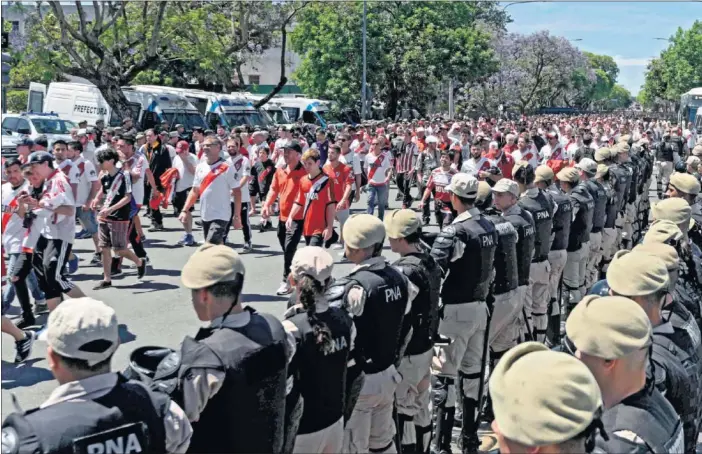  ??  ?? SEGURIDAD REFORZADA. Los aficionado­s de River Plate caminan por los alrededore­s del estadio Monumental de Núñez en Buenos Aires observados por dos líneas de policías.